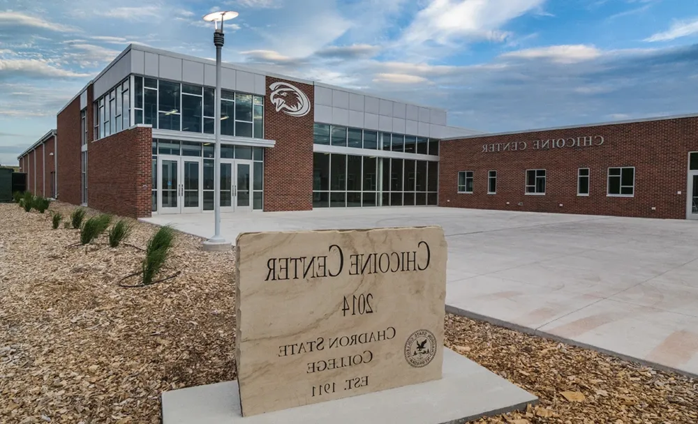 An athletic building of brick, 金属, 和玻璃, with a sign in the foreground reading Chicoine中心, 2014, Chadron State College, 美国东部时间. 1911